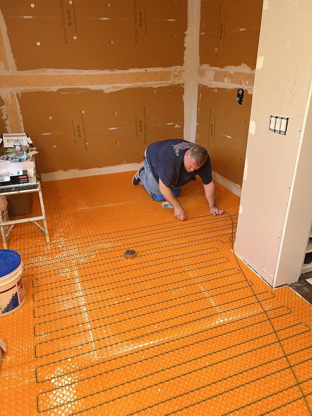 A man is kneeling on a tiled floor in a bathroom.