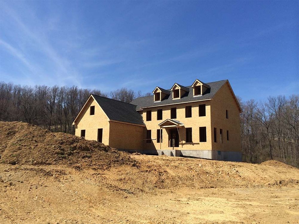 A large house is being built in the middle of a dirt field.