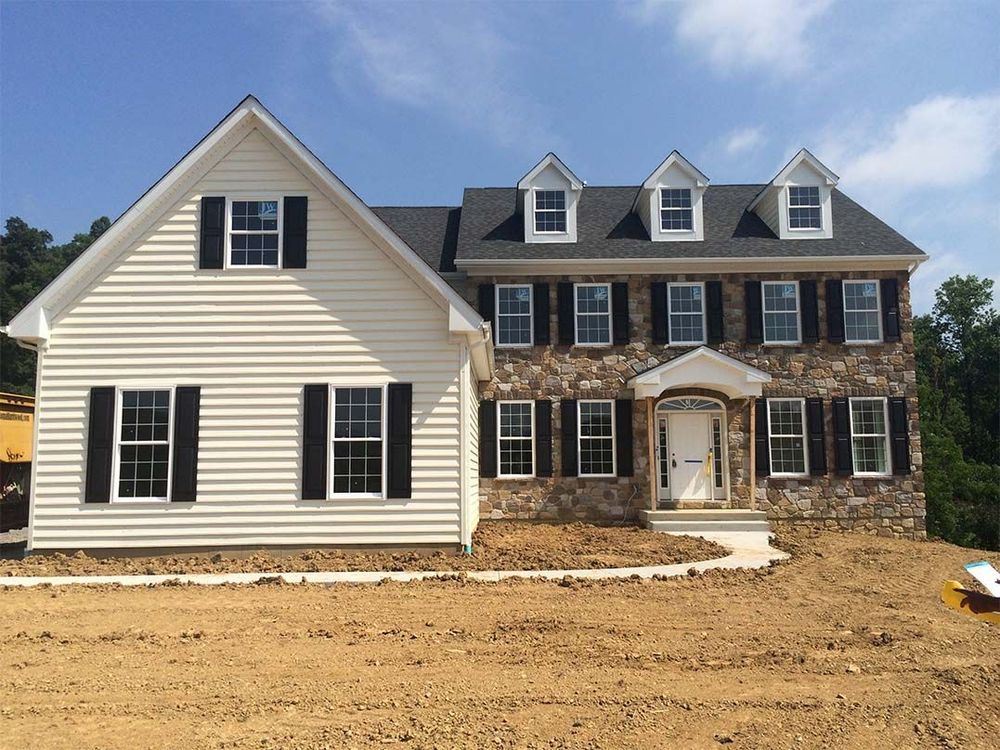 A large white house with black shutters sits on top of a dirt field