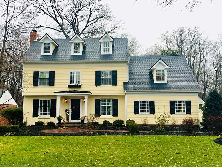 A large yellow house with black shutters and a blue roof