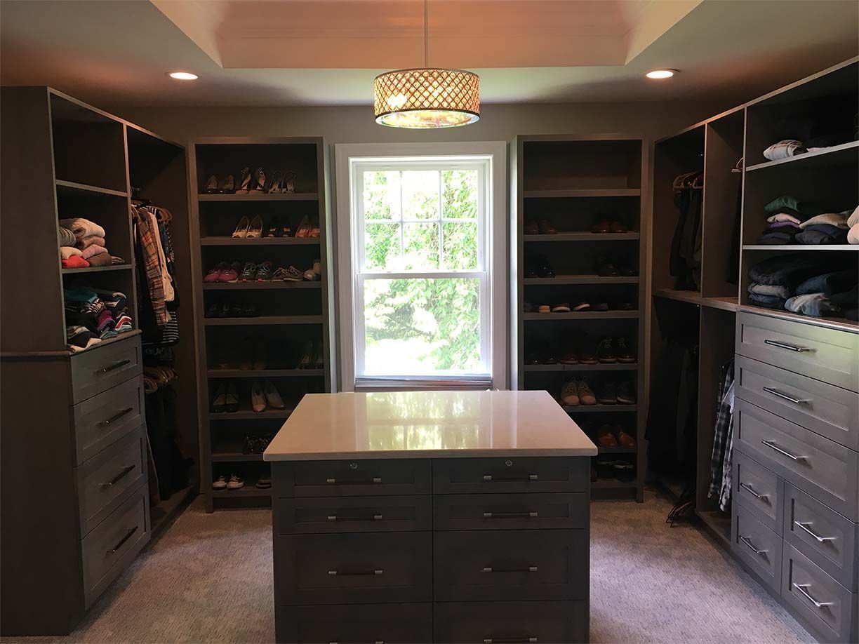 A walk in closet with lots of shelves and drawers and a large island in the middle.