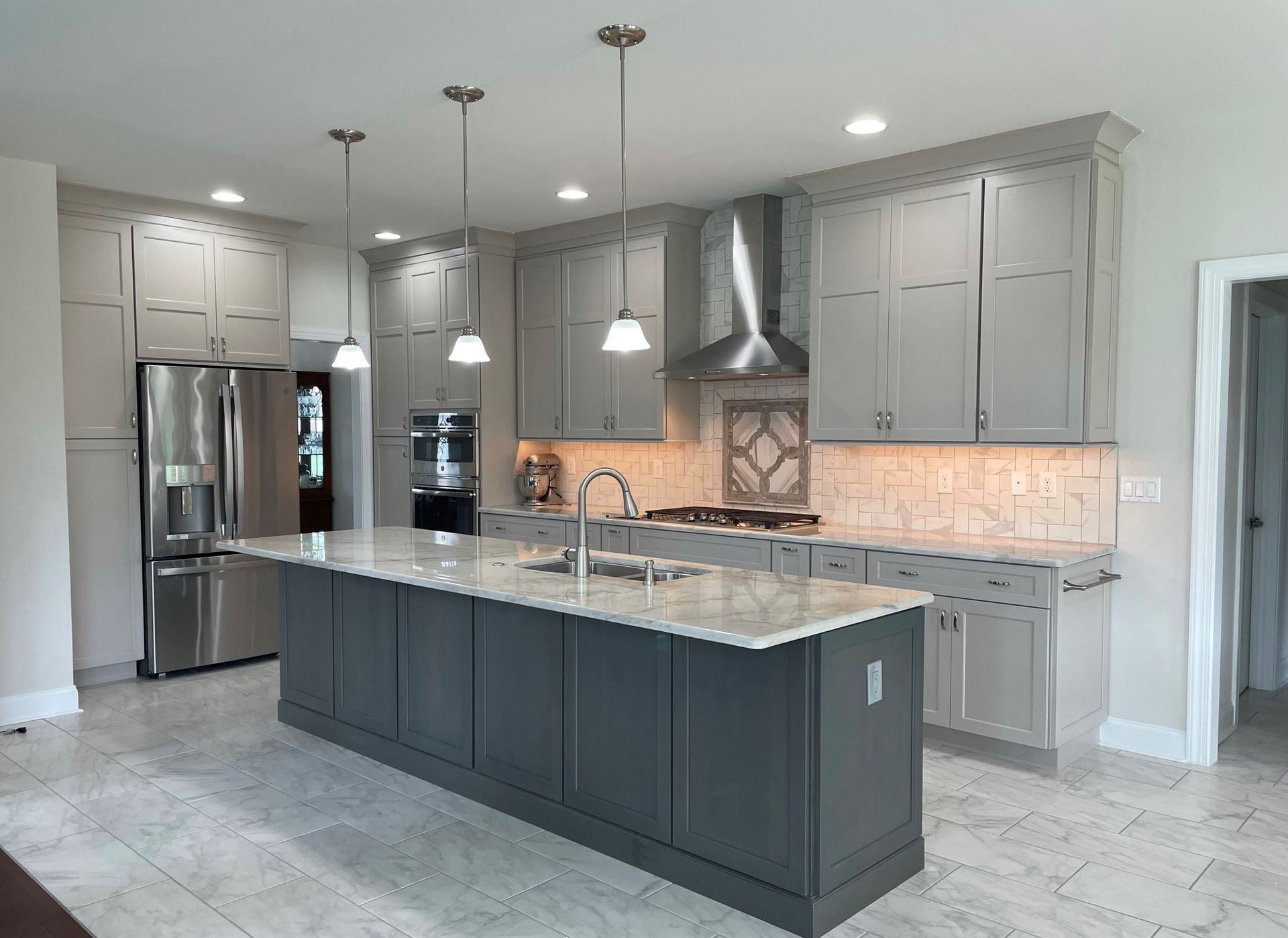 A kitchen with gray cabinets , granite counter tops , stainless steel appliances and a large island.