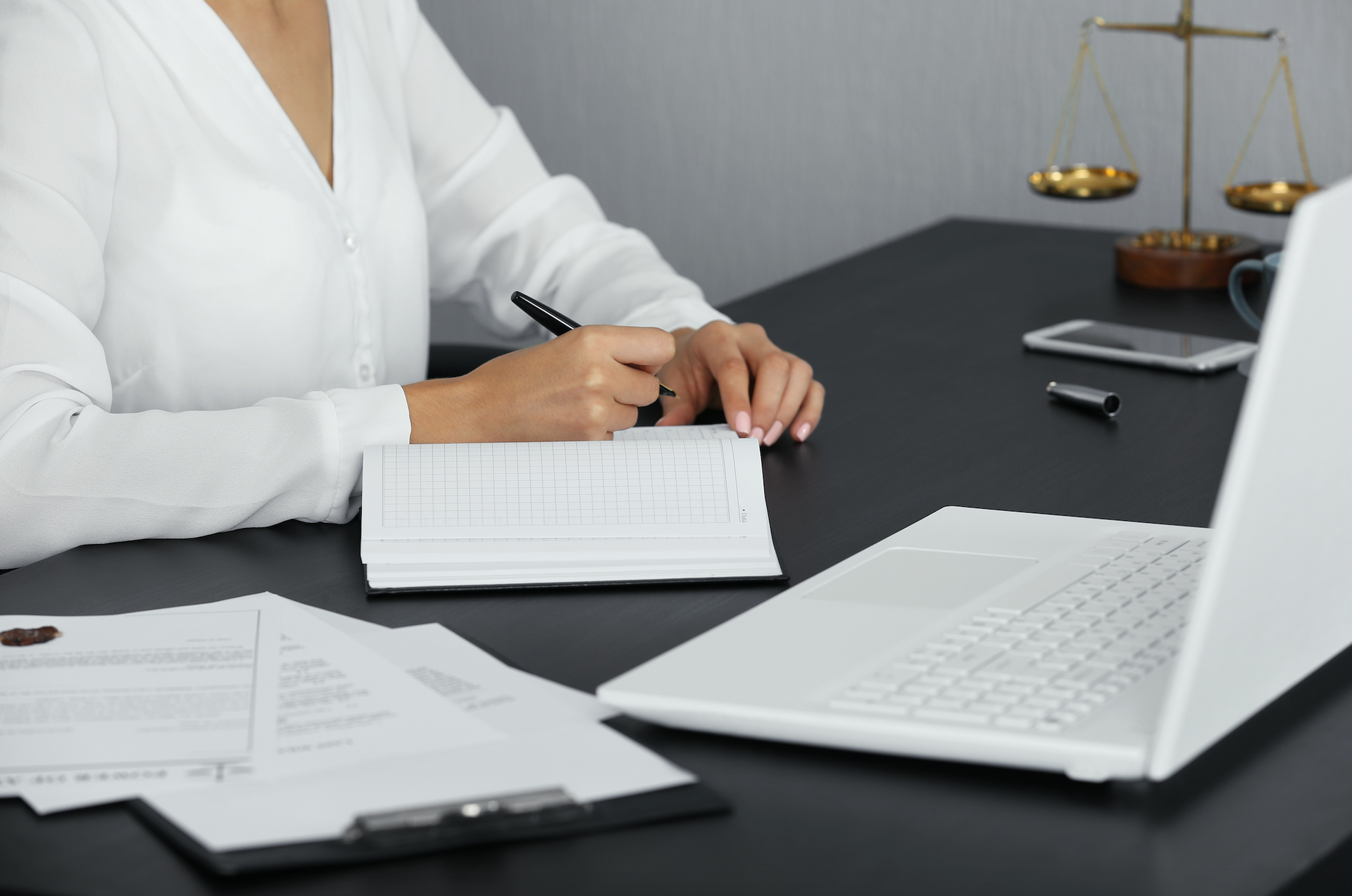 A woman is sitting at a desk with a laptop and a notebook.