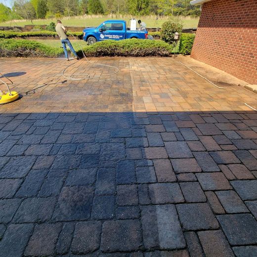 A man is cleaning a brick driveway with a pressure washer.