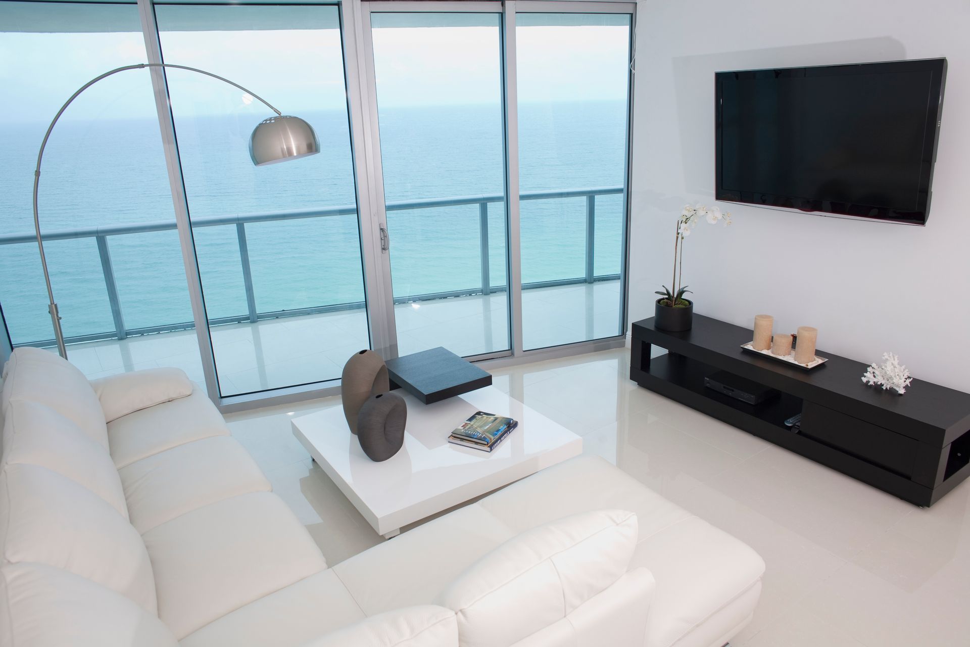 Modern living room with ocean view, white furniture, TV, and floor lamp.