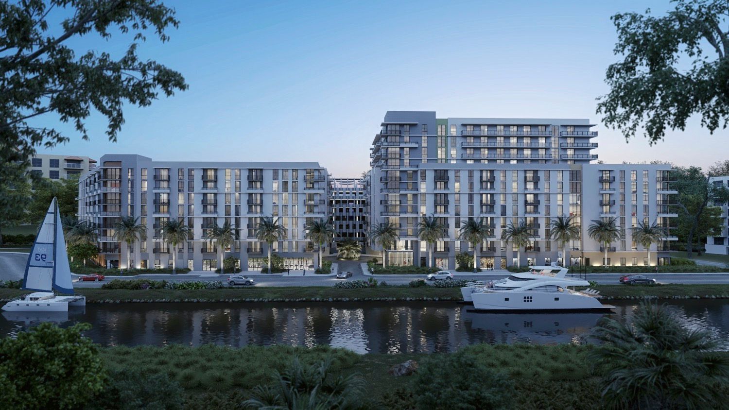 Modern waterfront apartment buildings at dusk, with boats and landscaping in the foreground.