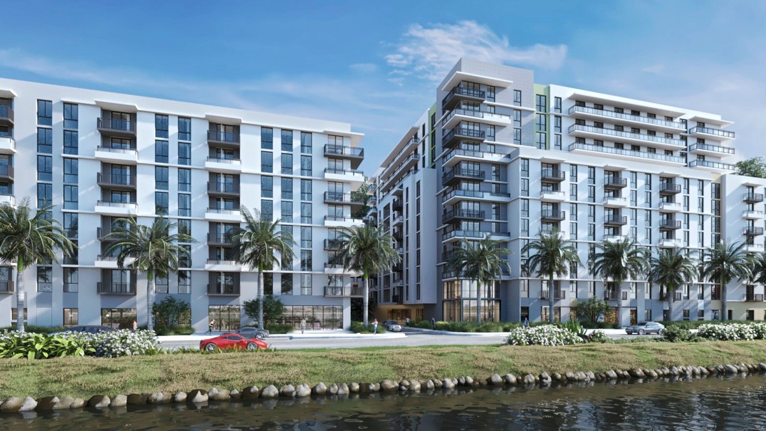 Modern apartment buildings next to a waterway with palm trees under a blue sky.