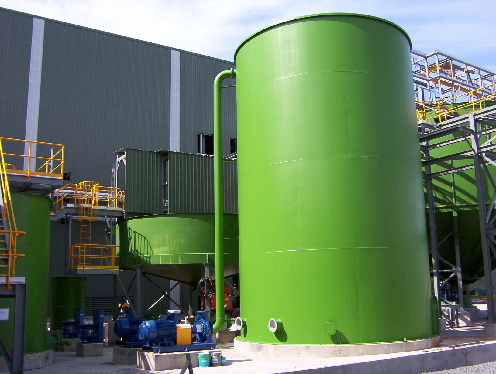 Large green industrial tank outside a building, pipes and machinery visible.