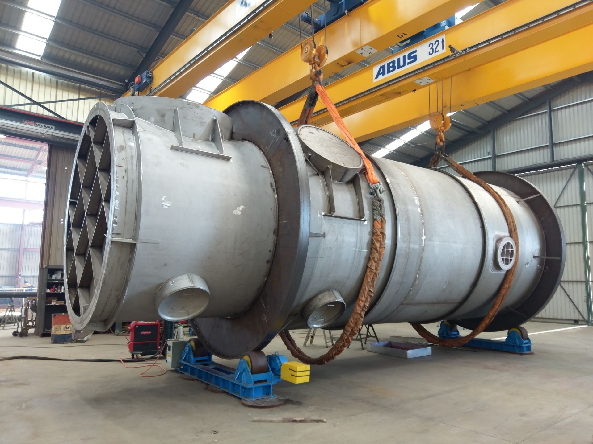 Large cylindrical industrial vessel being lifted by a crane inside a factory.