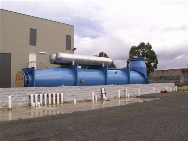 Blue industrial water treatment equipment outside a building, with silver tanks on top, near a wet surface.