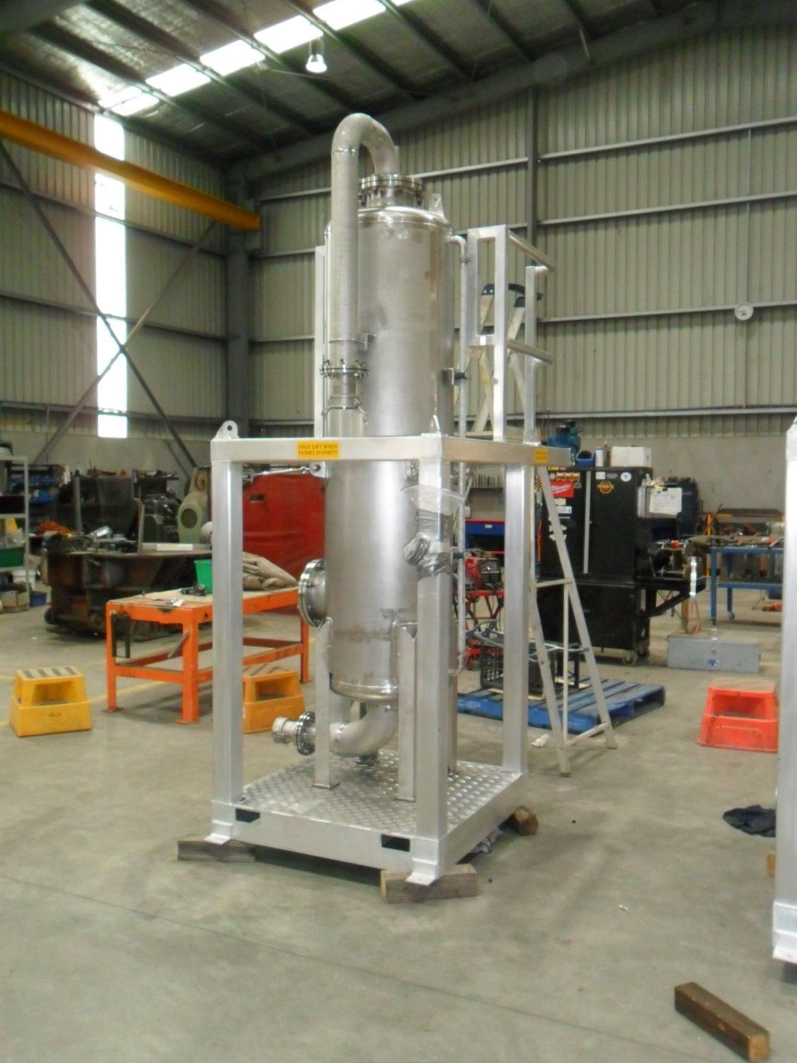 Stainless steel industrial vessel within a metal frame, inside a factory.