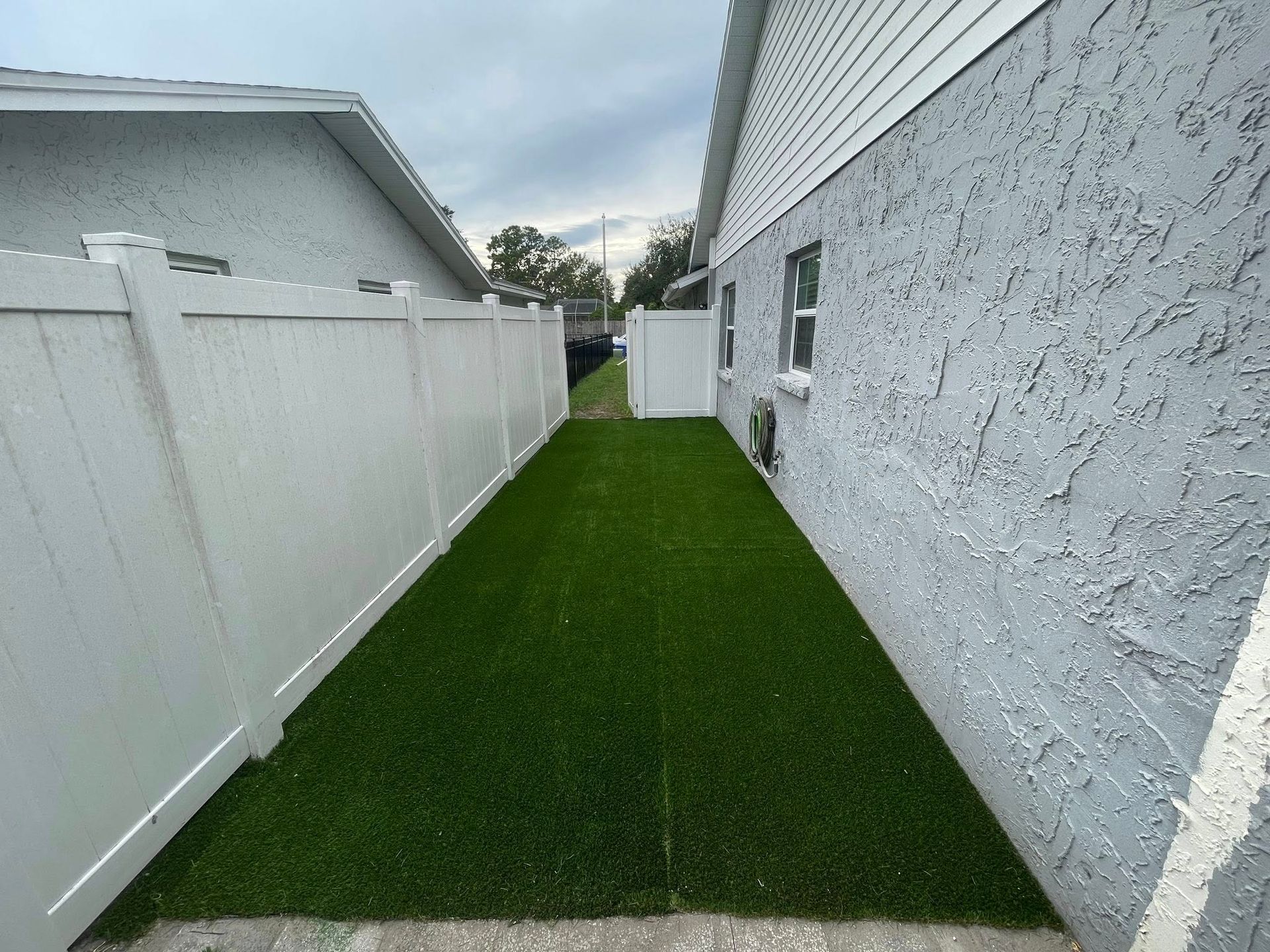 Narrow backyard with white fence, green turf, and stucco wall.