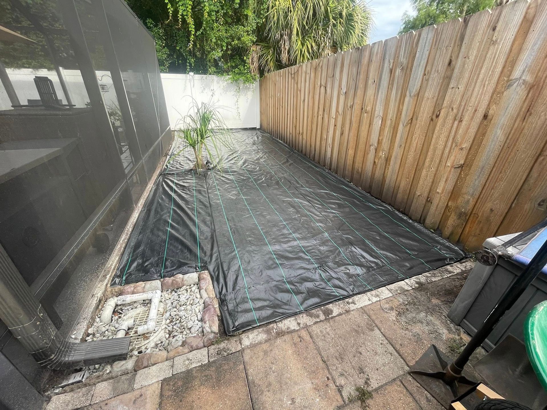 Black weed barrier covers a prepared garden bed next to a wooden fence.