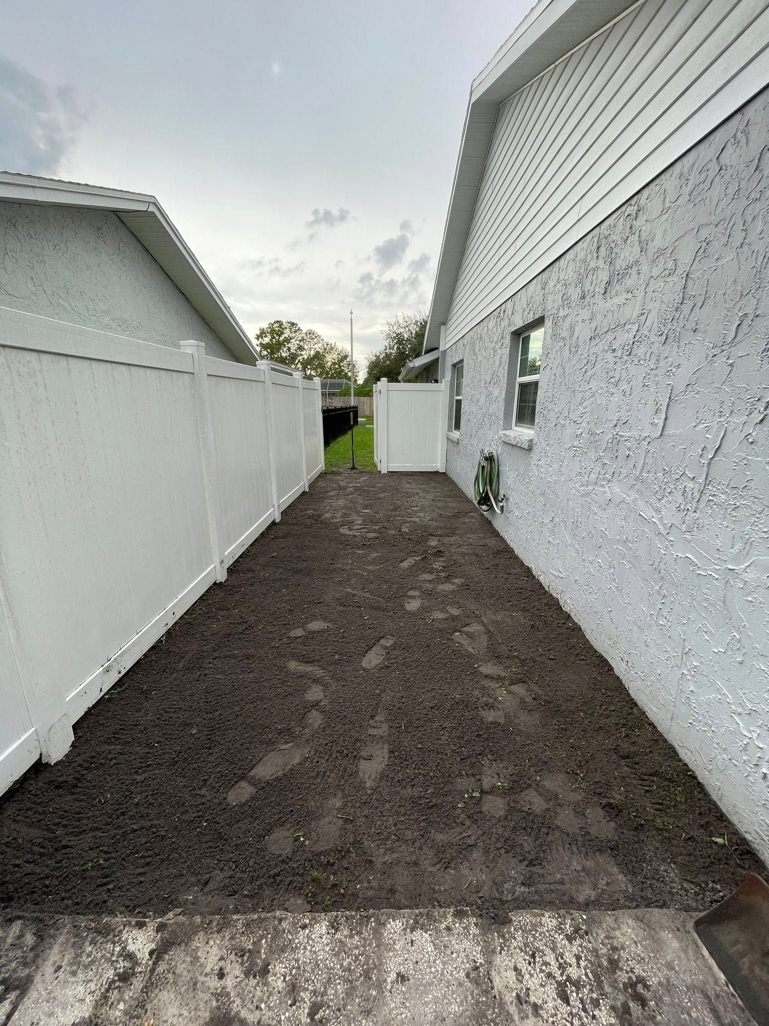 Narrow gravel pathway between a white fence and a stucco wall, leading to a small gate.