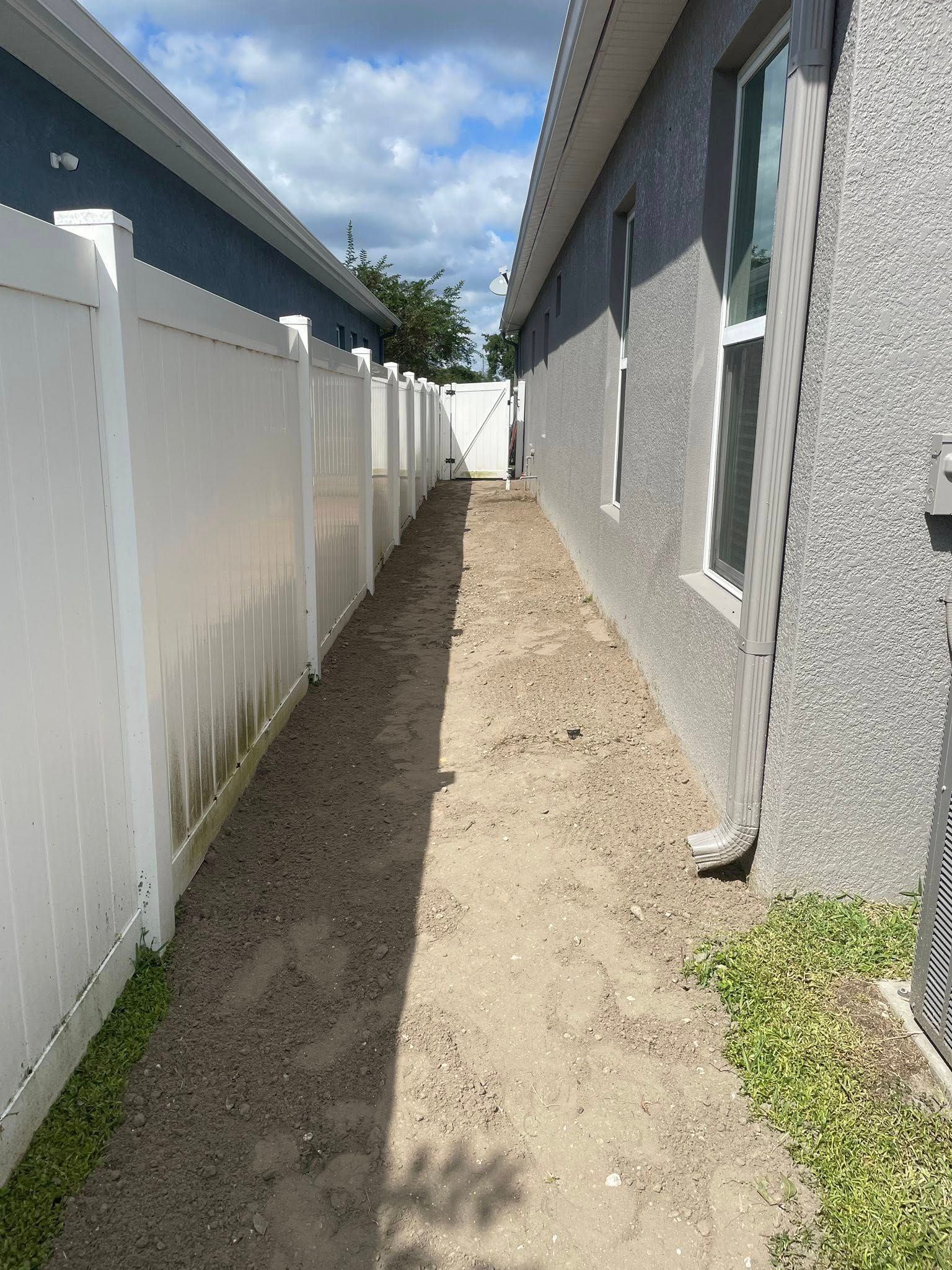 Narrow gravel walkway between a white fence and a gray stucco wall, leading to a gate.