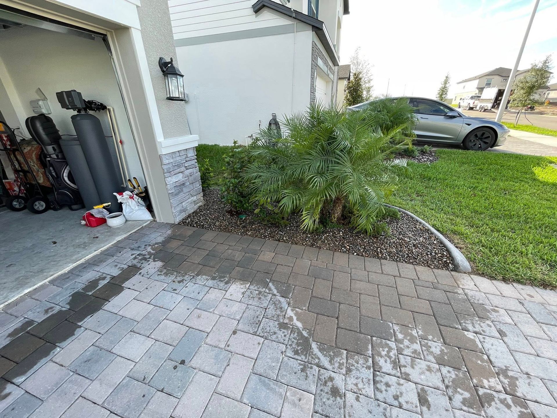 Driveway with wet pavers, a garage, landscaping, and a parked car.