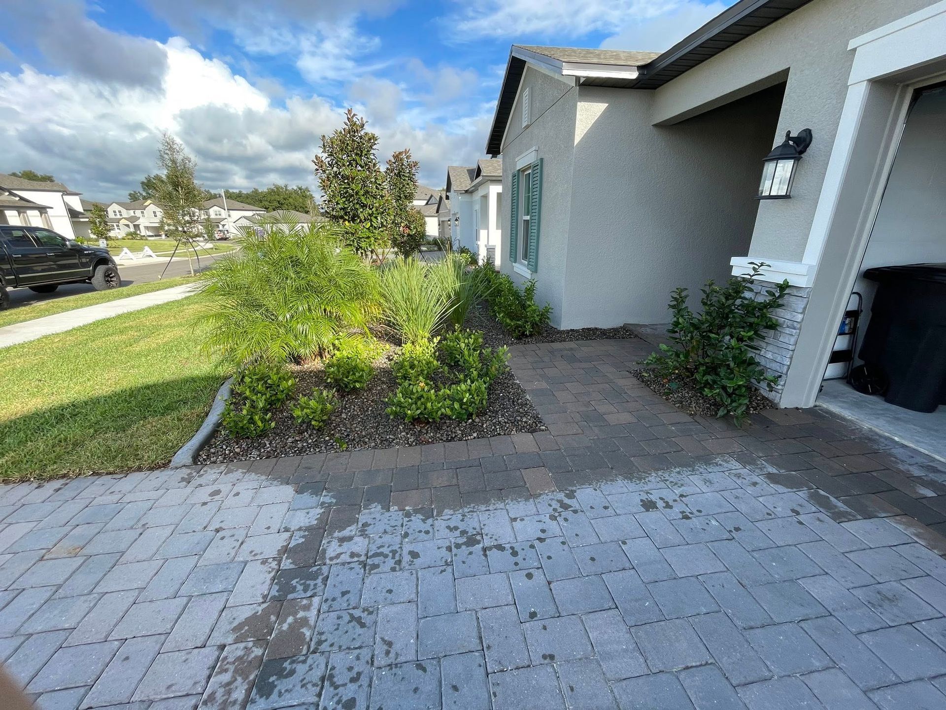 A house exterior with a paved driveway and landscaped yard. Green bushes and trees are in the yard.