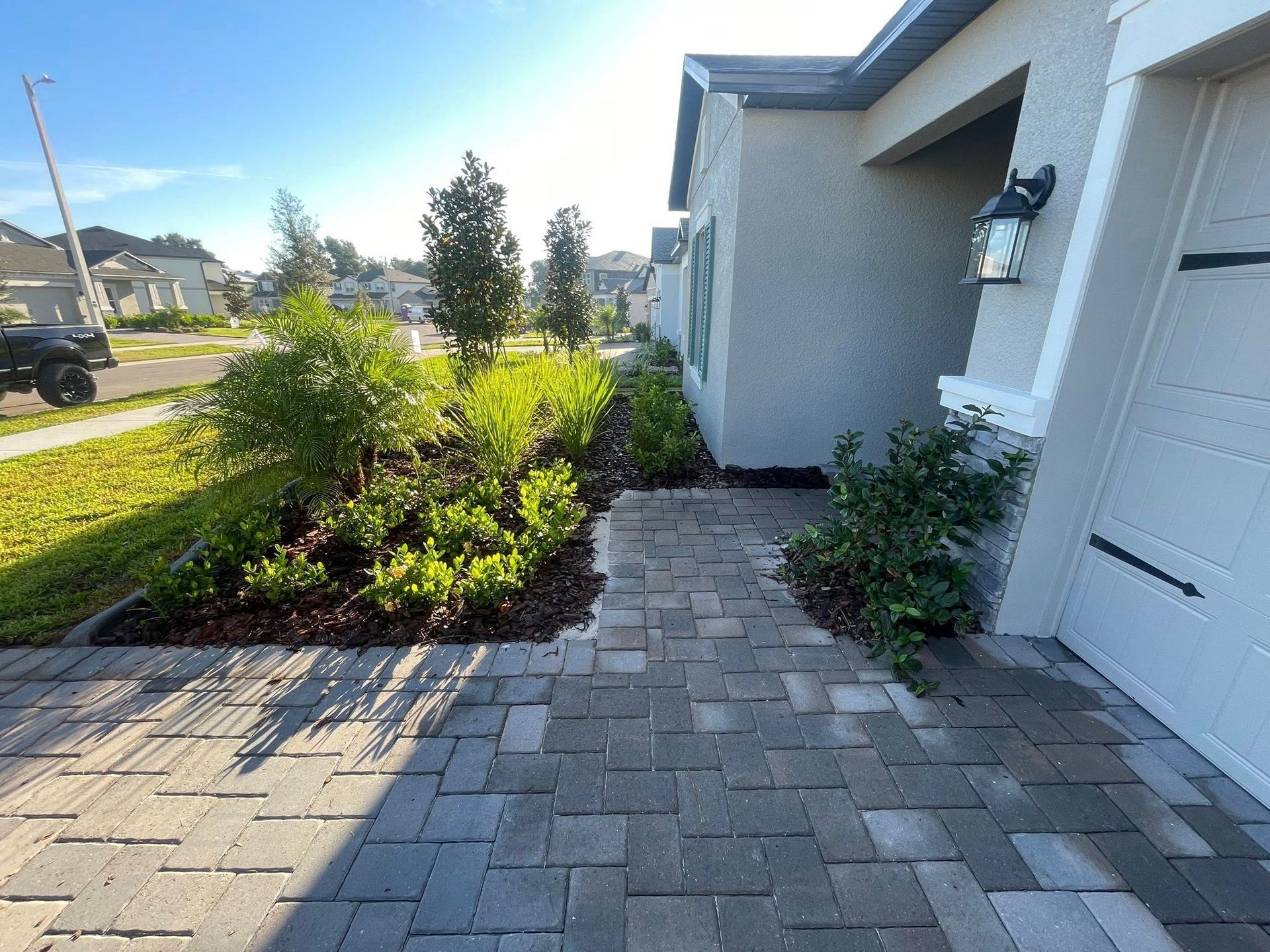 Paved walkway leads to a beige house, with landscaping. Garage and driveway are on the right.