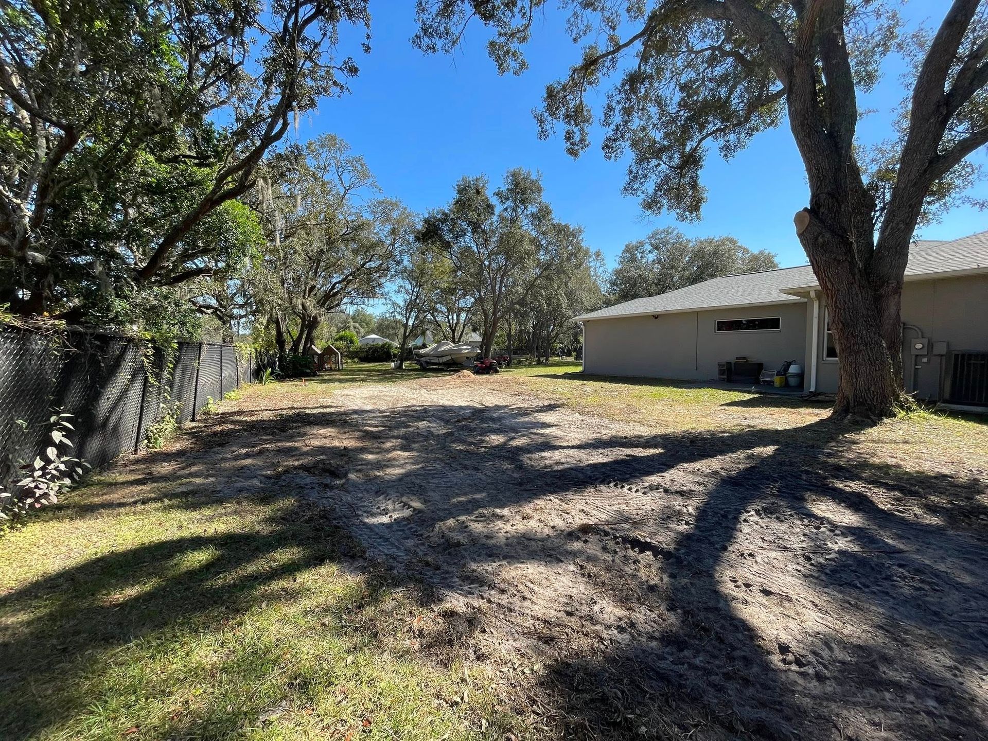 Cleared lot with dirt and grass, bordered by fence and house under a sunny sky.