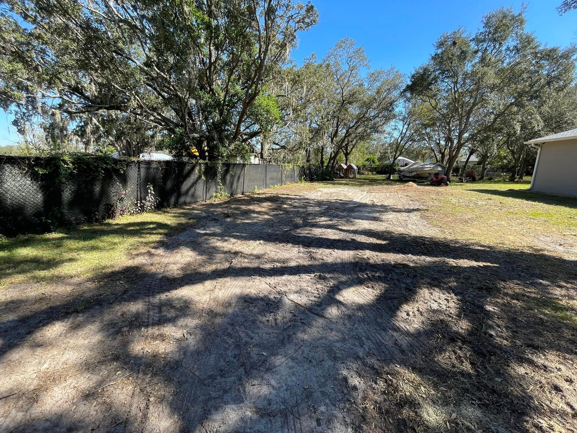 Gravel driveway leading to a grassy area with trees and a black fence under a blue sky.