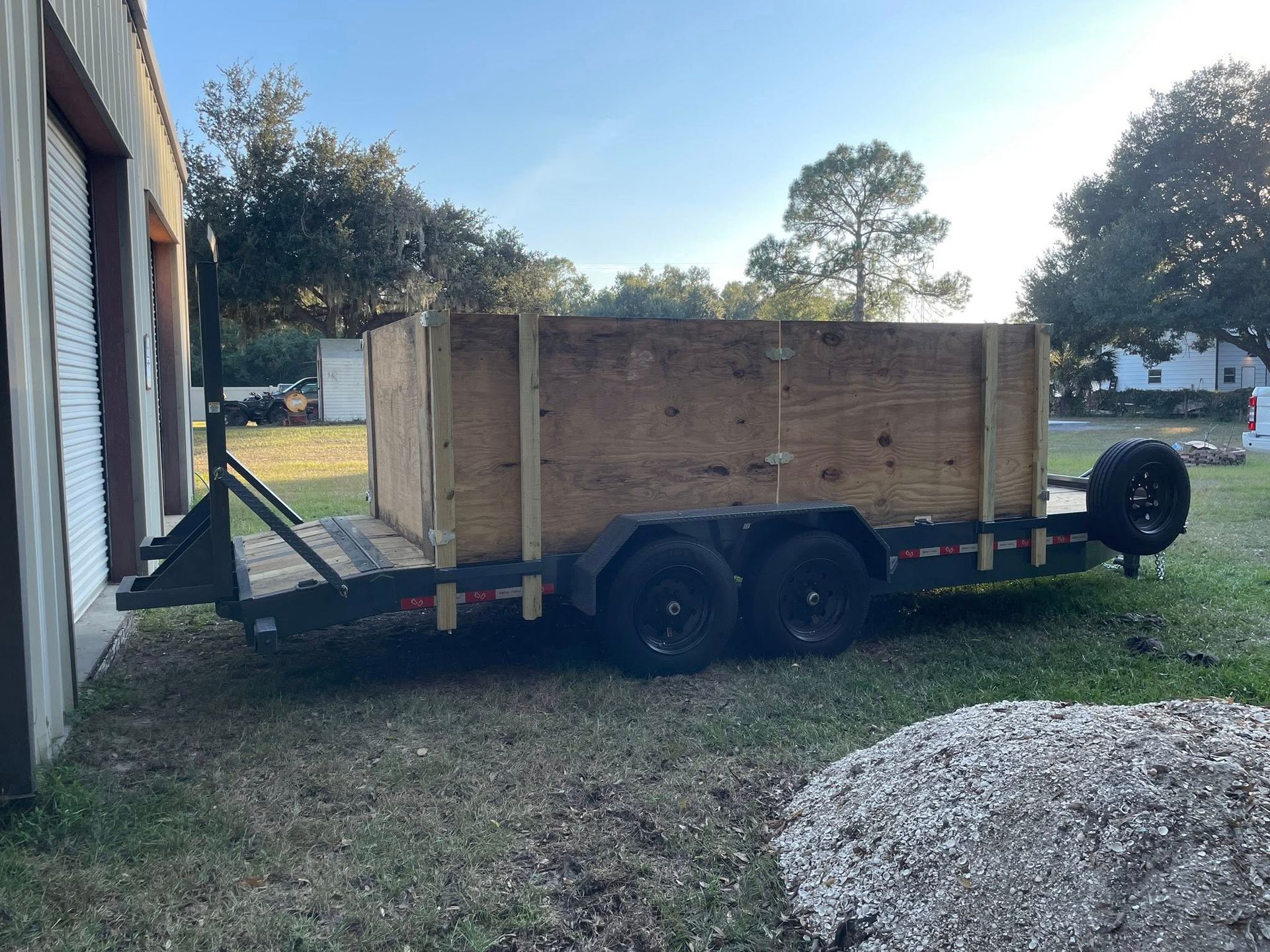 Trailer with plywood box, parked on grass near a building.
