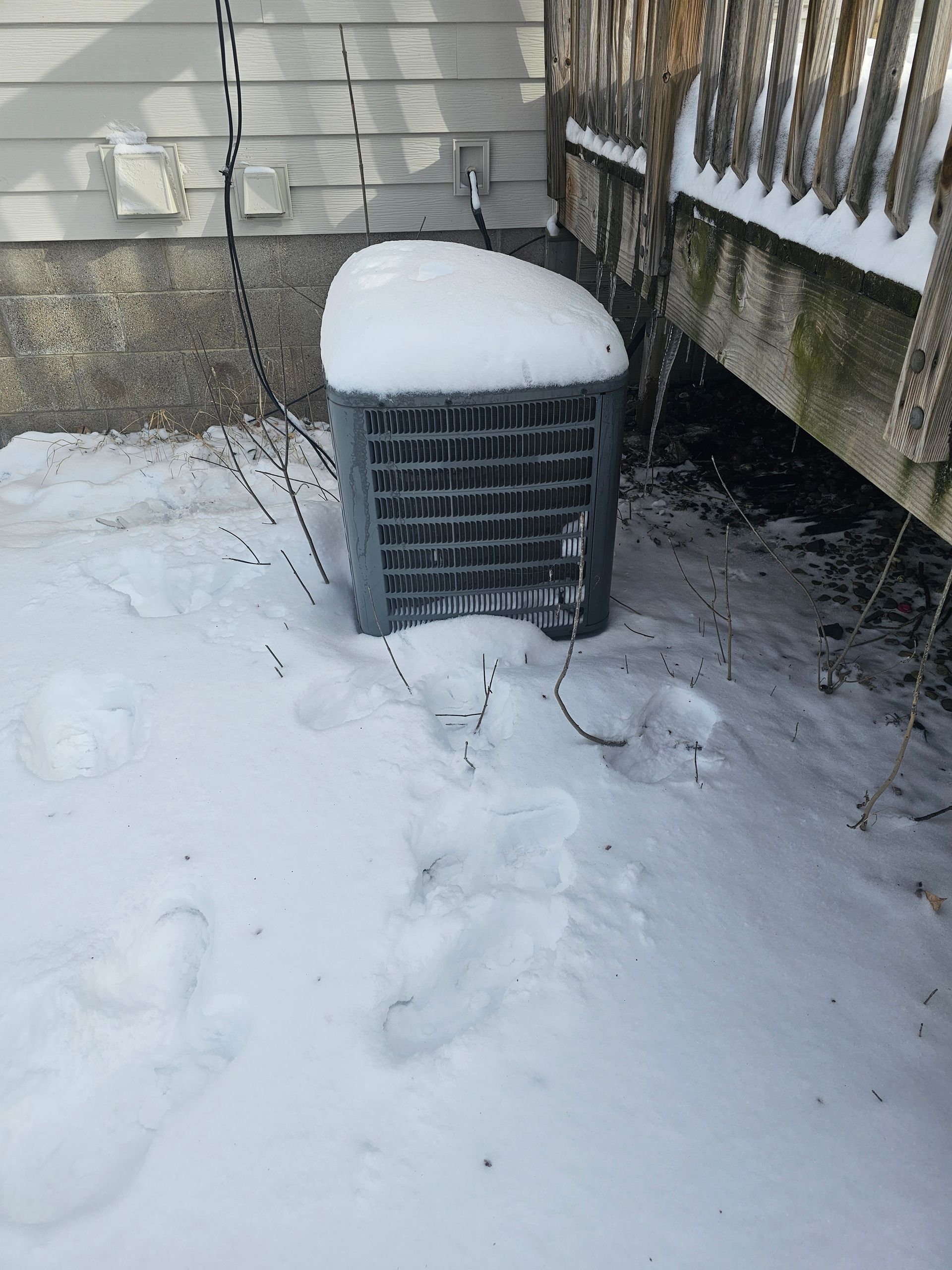 An air conditioner is covered in snow in front of a house.