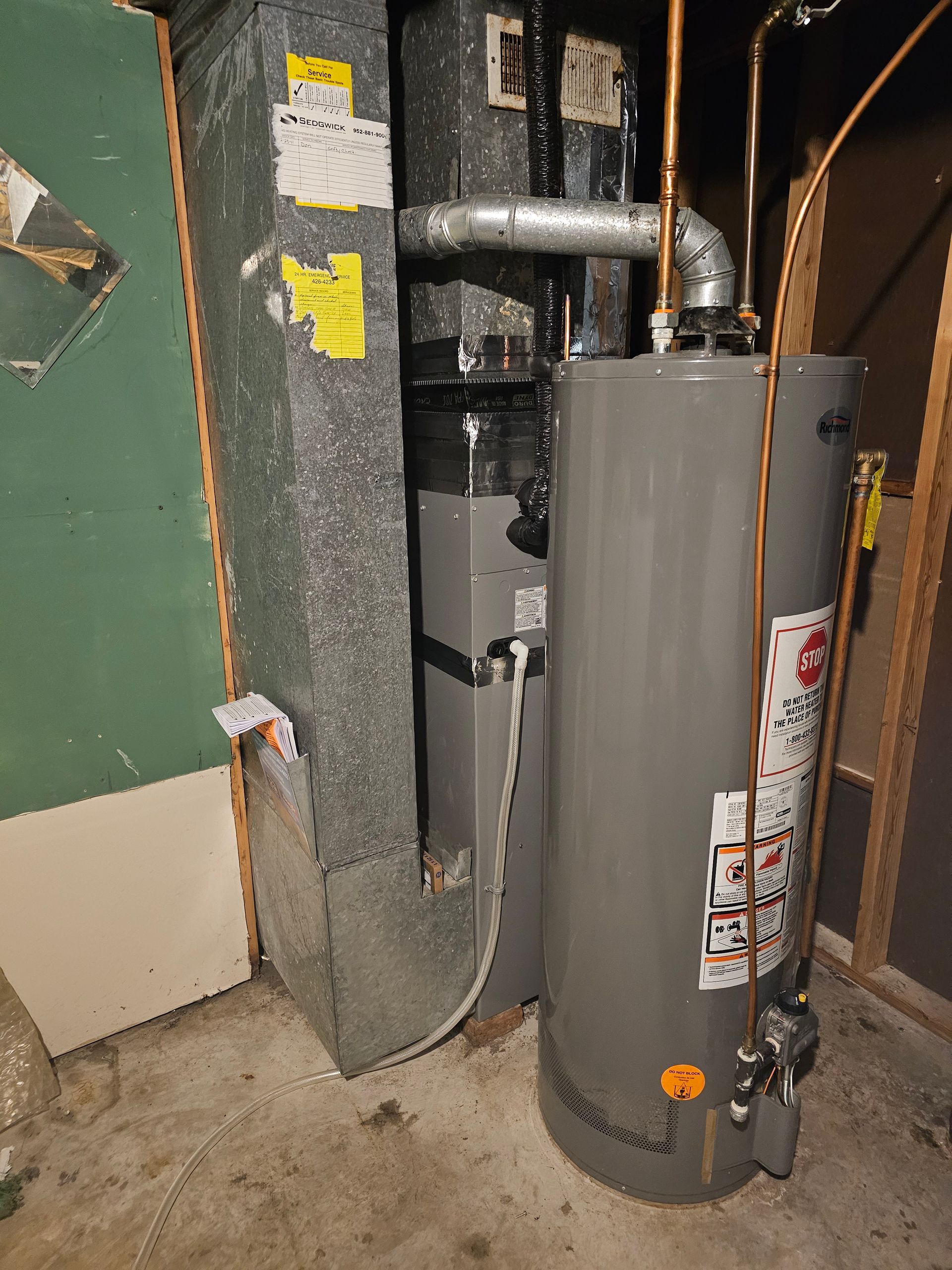 A water heater is sitting next to a furnace in a basement.