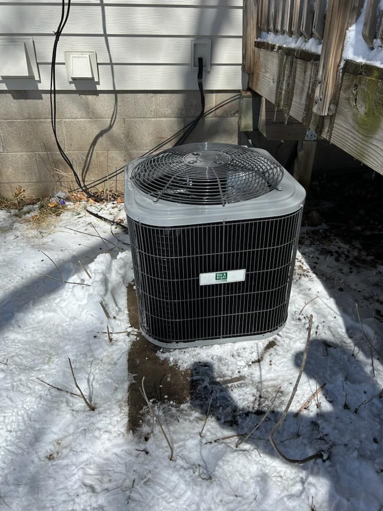 An air conditioner is sitting in the snow outside of a house.
