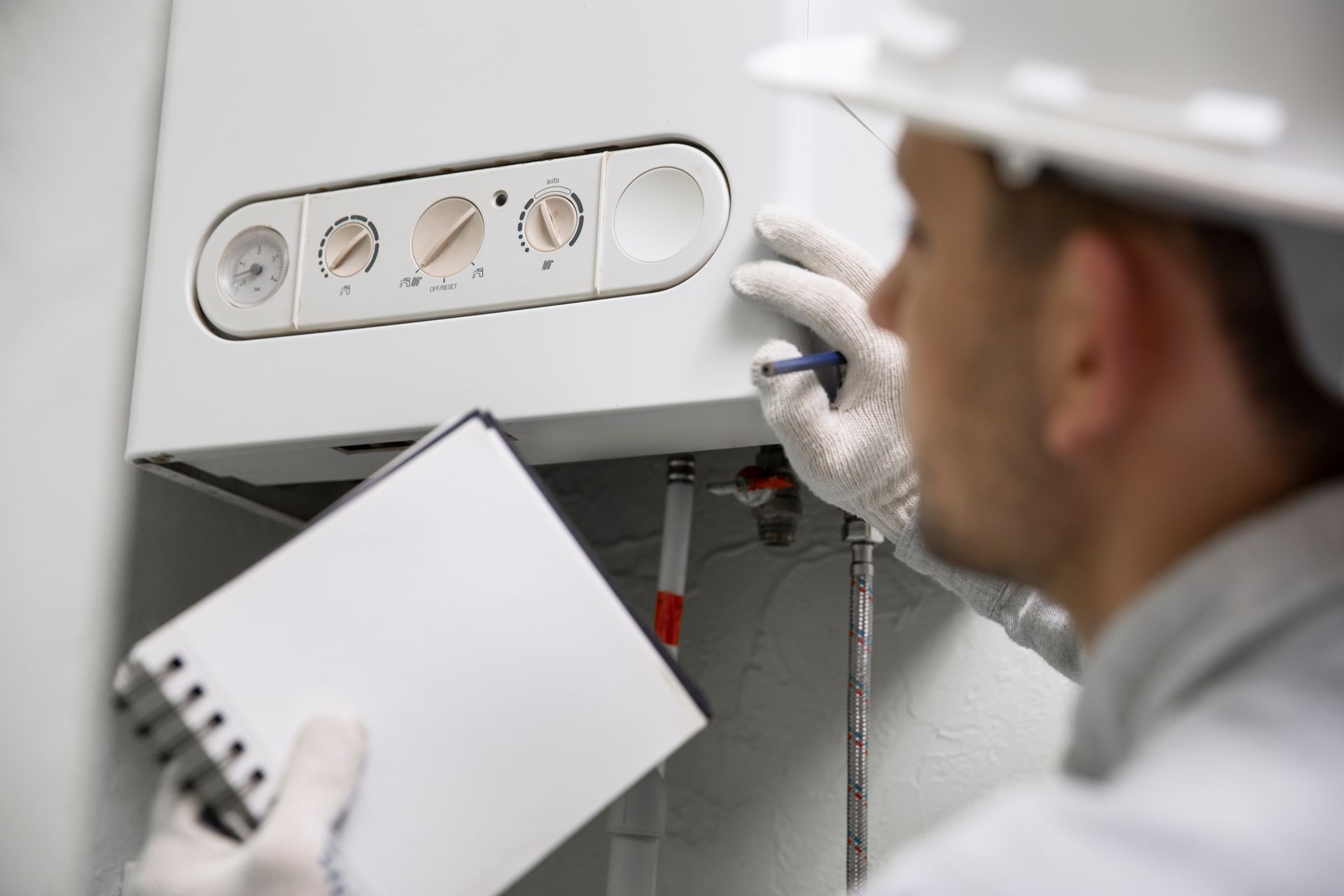 Technician in a hard hat inspecting a white boiler, holding a notepad.