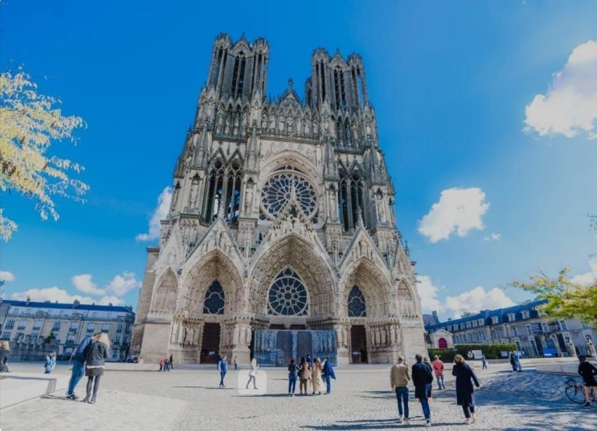 Un bus est stationné dans une rue de la ville ; des passagers descendent. Un bâtiment historique et des piétons se trouvent sur le trottoir.