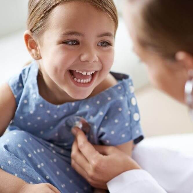 Child smiling as a doctor listens to their chest with a stethoscope.