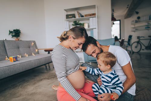 Pregnant woman, partner, and child on floor, touching belly, living room.