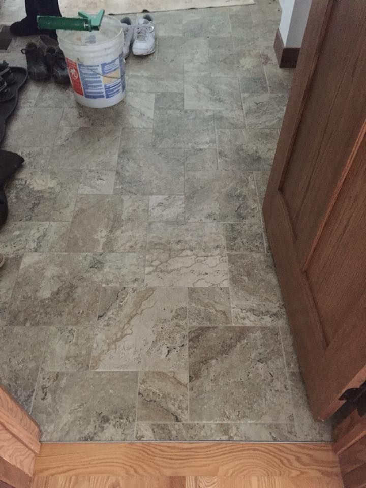 A bucket of paint is sitting on a tiled floor next to a door.