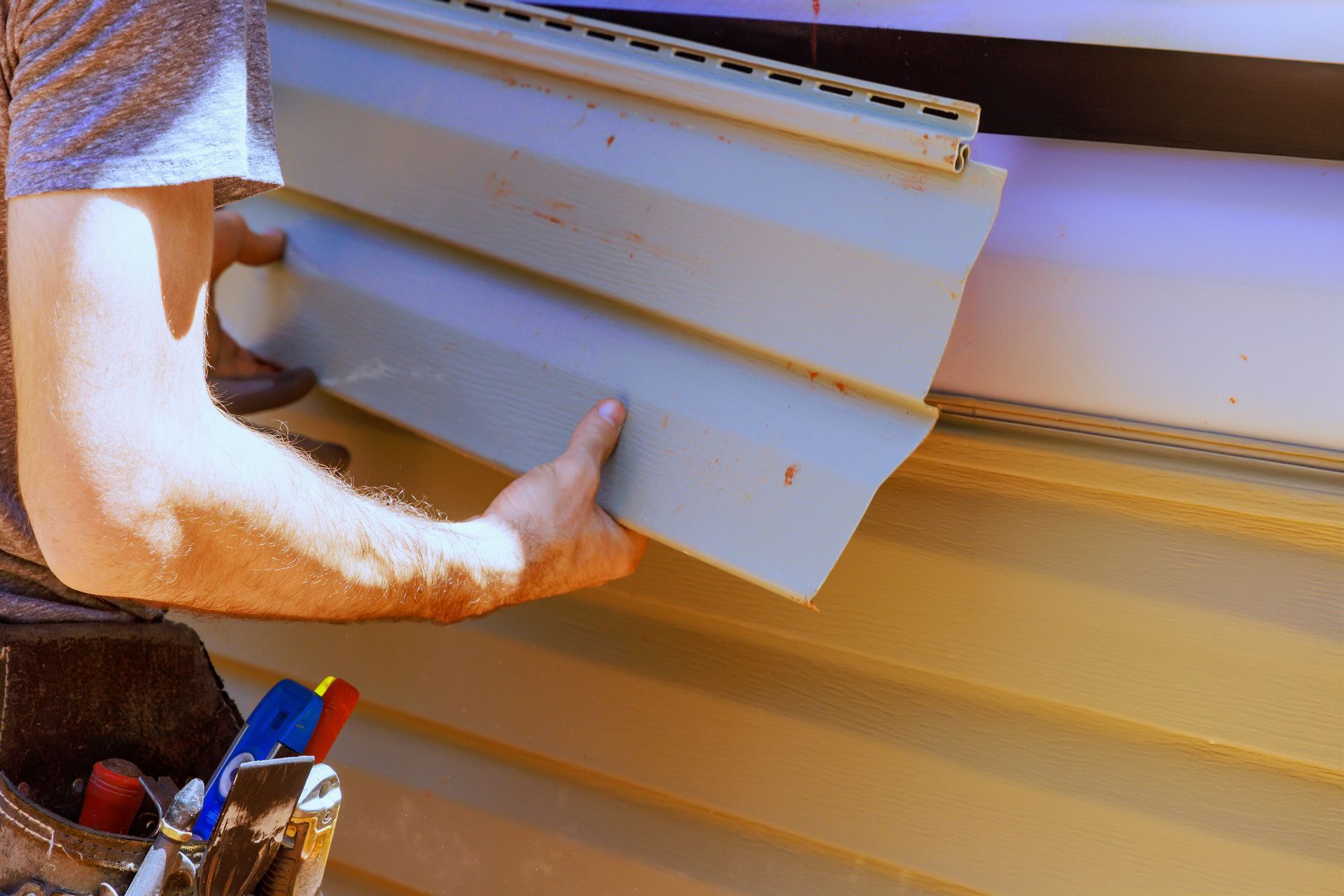As part of construction, a worker installs vinyl siding panels on a house facade.