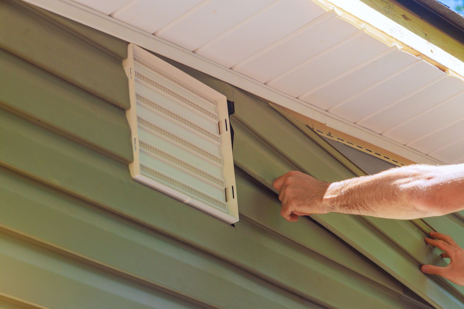 Construction employee installs vinyl plastic siding panels on the facade of a new house.