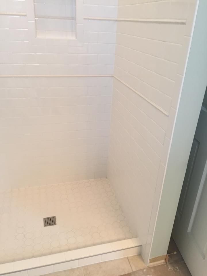 A shower stall with a glass door and white tiles in a bathroom.