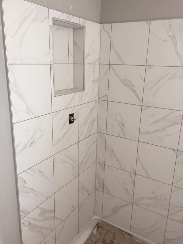 A bathroom with white tiles and a shelf in the corner.