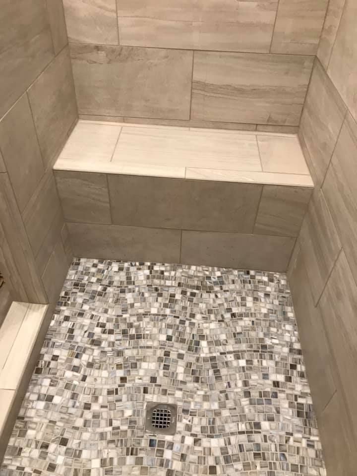 A shower with a mosaic tile floor and a drain.