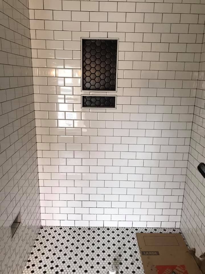 A bathroom with white tiles and a black and white tile floor.