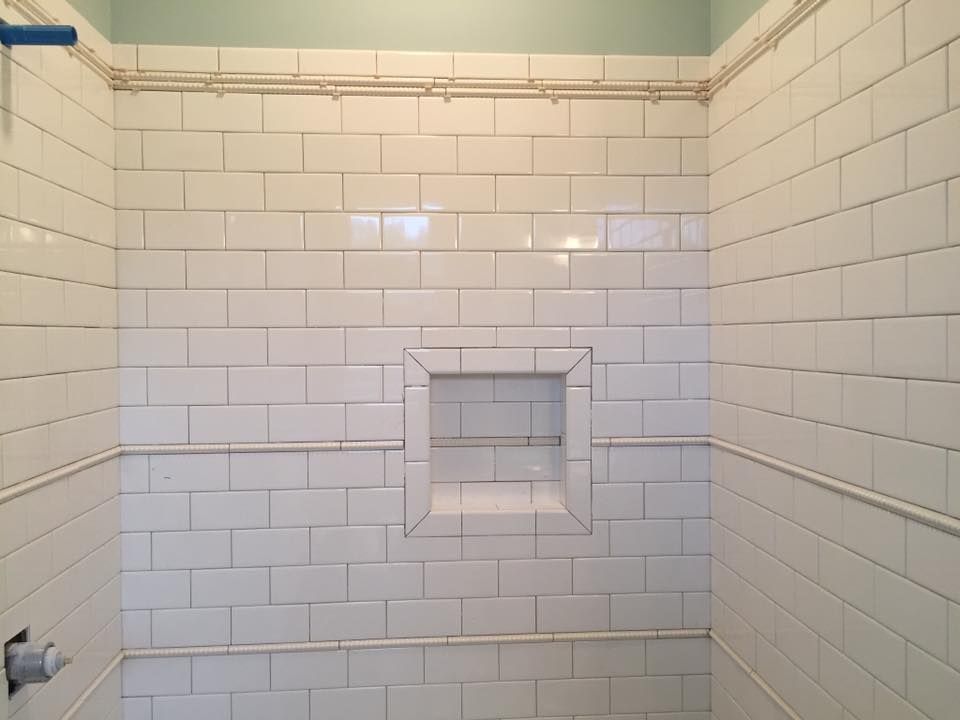 A bathroom with white tiles and a shelf