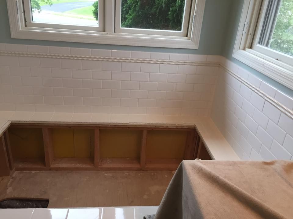 A bathroom with a window and a bench in the corner.