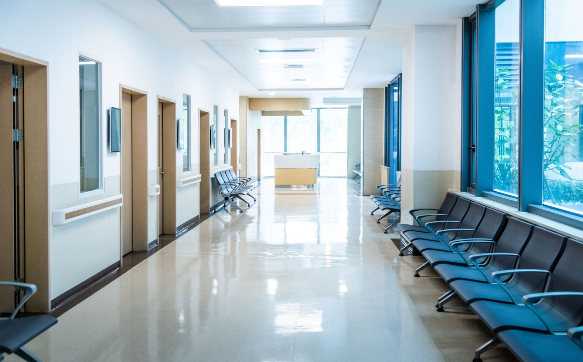 Empty hospital corridor with blue chairs, doors, and bright windows