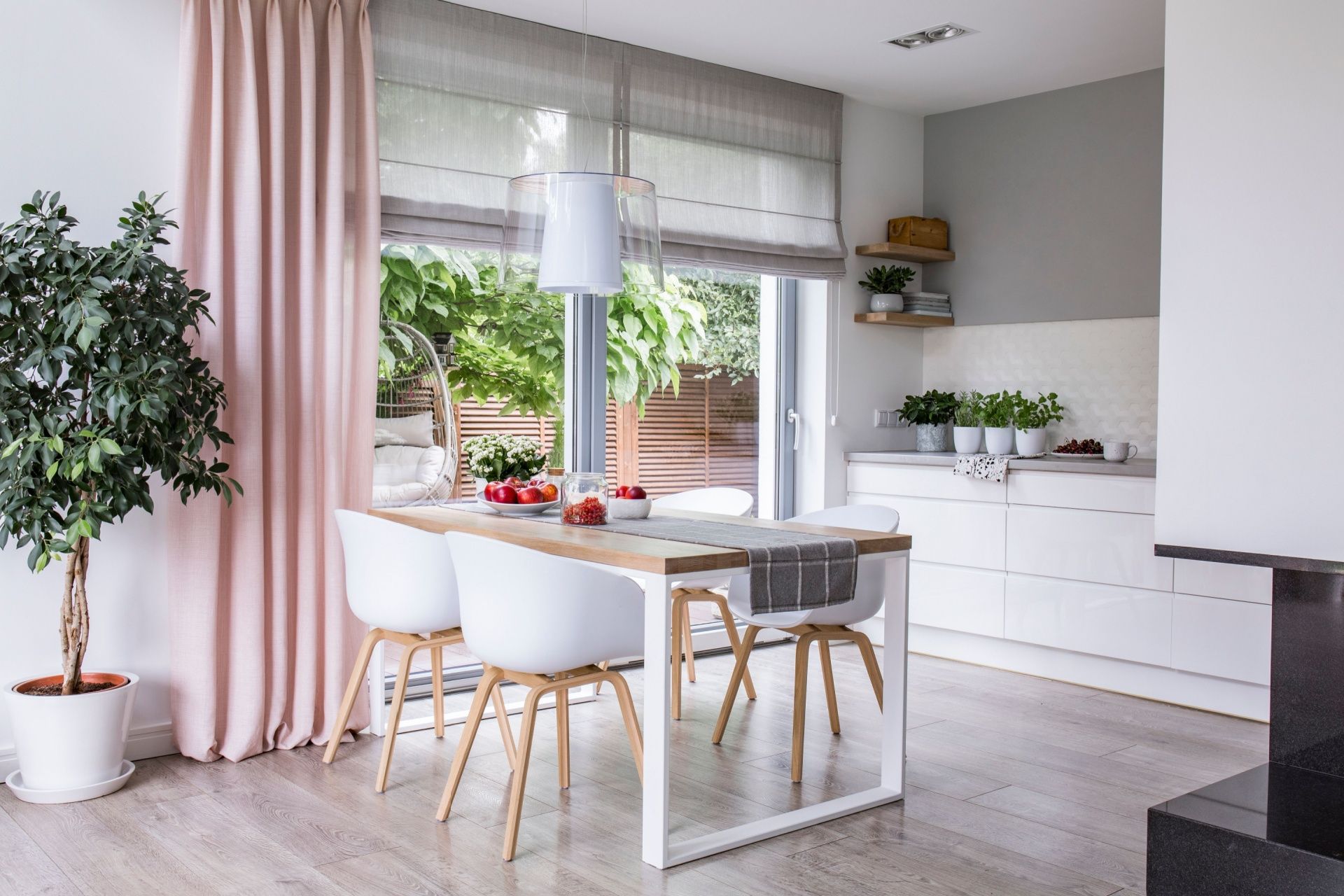 Bright dining area with white table and chairs, pink curtains, and a garden view through large windows