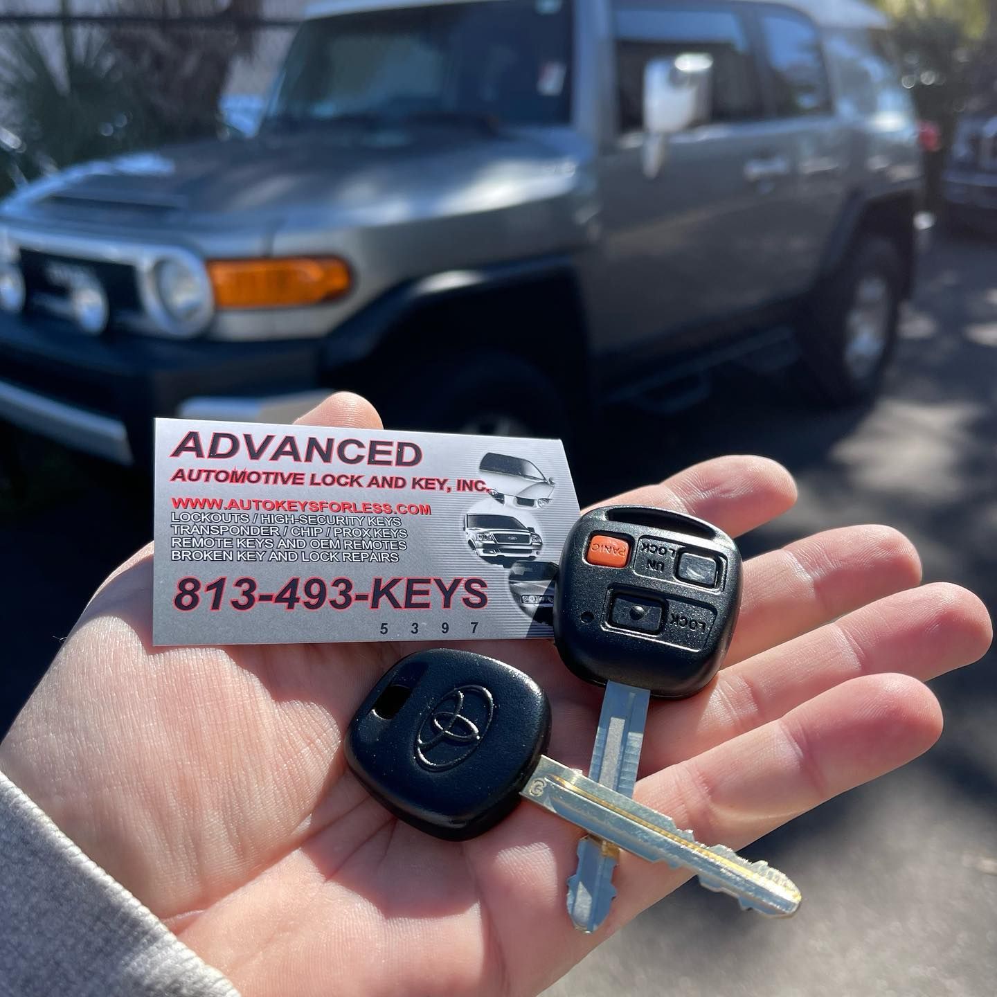 A person is holding a car key and a business card in front of a car.