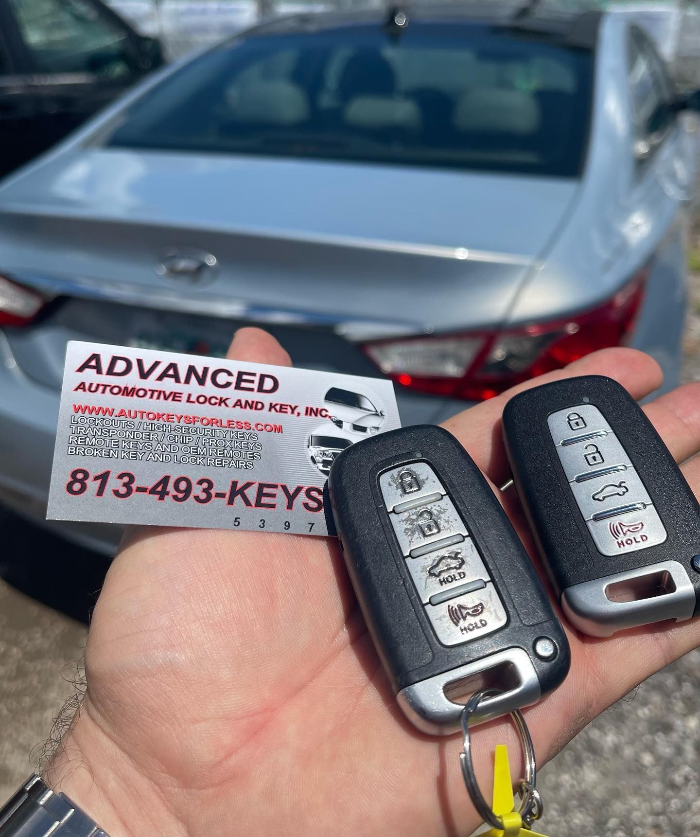 A person is holding two remote keys in front of a car.