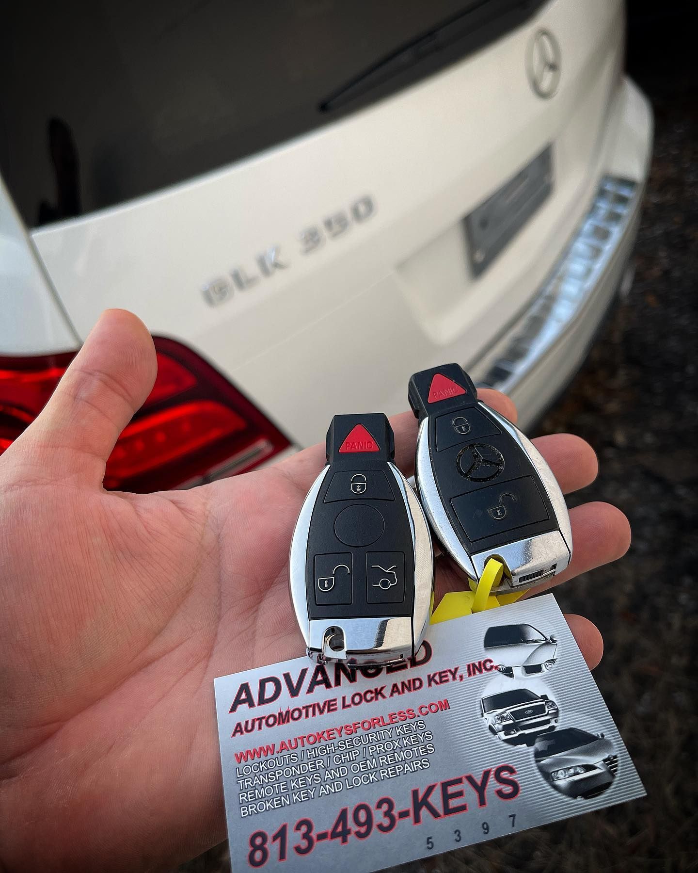 A person is holding a pair of keys in front of a white mercedes