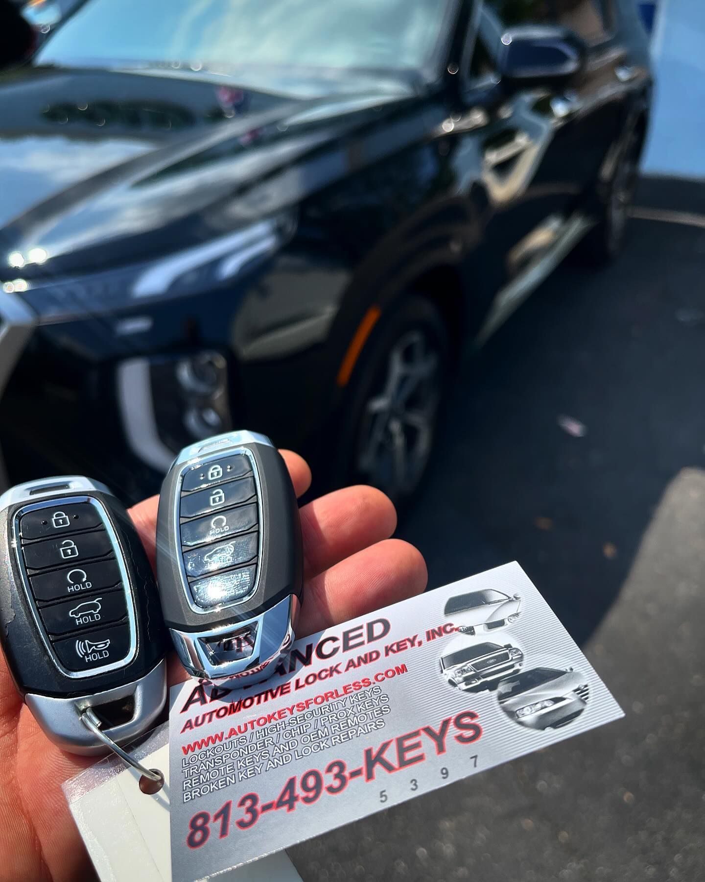 A person is holding two remote keys in front of a car.