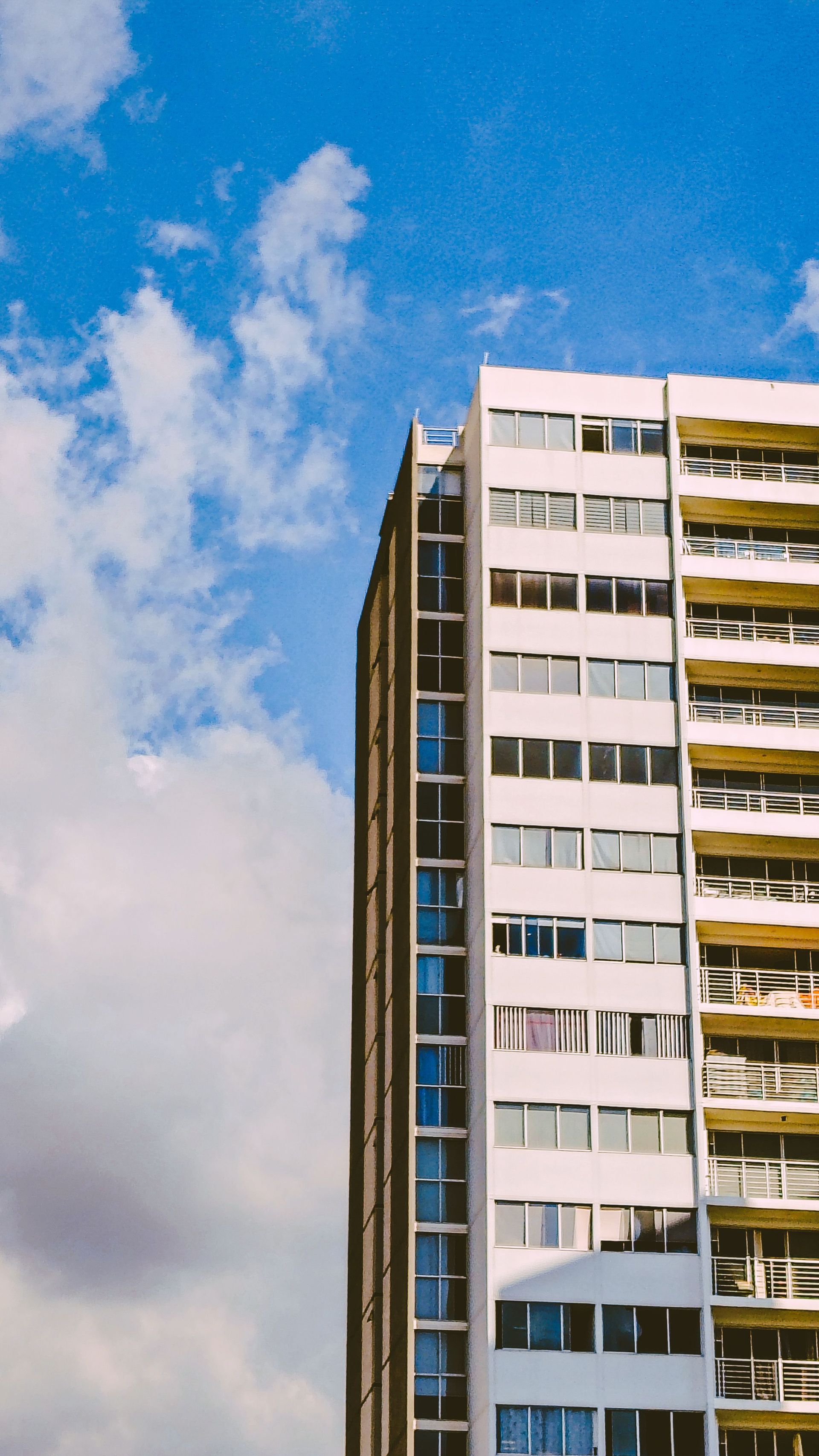 Tall white apartment building against a bright blue sky with scattered clouds