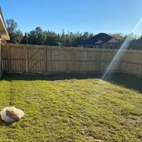 Wooden fence enclosing a grassy backyard under a bright blue sky.