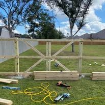 Wooden fence construction in a grassy yard, with lumber and tools nearby.
